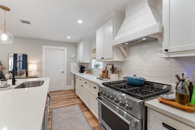 kitchen featuring a sink, stainless steel range, custom range hood, and white cabinetry