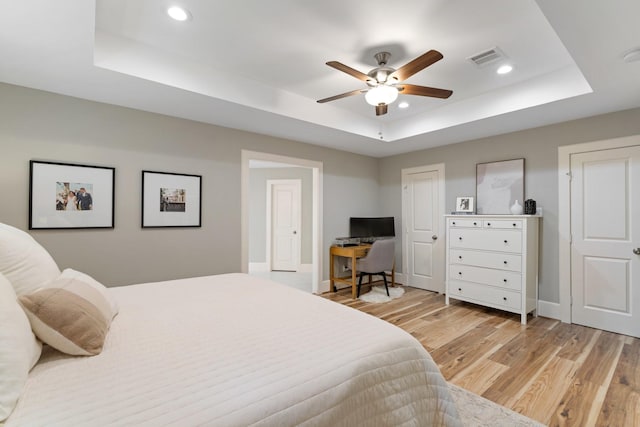 bedroom with light wood-style floors, a tray ceiling, recessed lighting, and visible vents