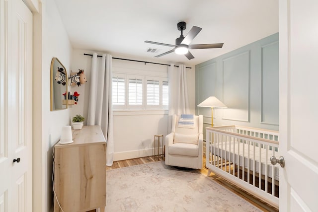 bedroom featuring a ceiling fan, visible vents, wood finished floors, a crib, and baseboards