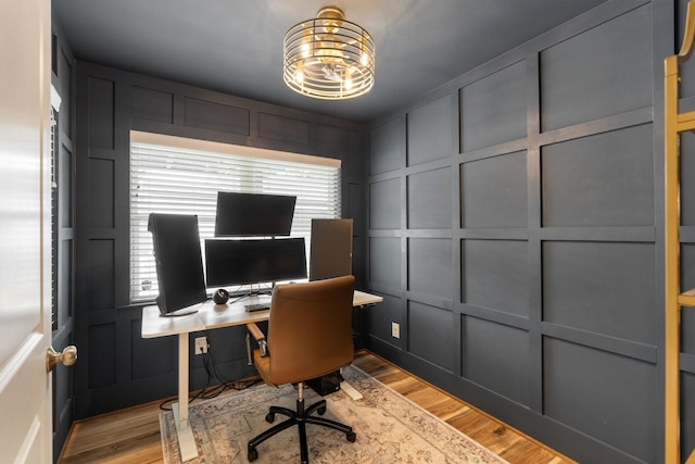 home office featuring light wood-style floors, a decorative wall, and a notable chandelier