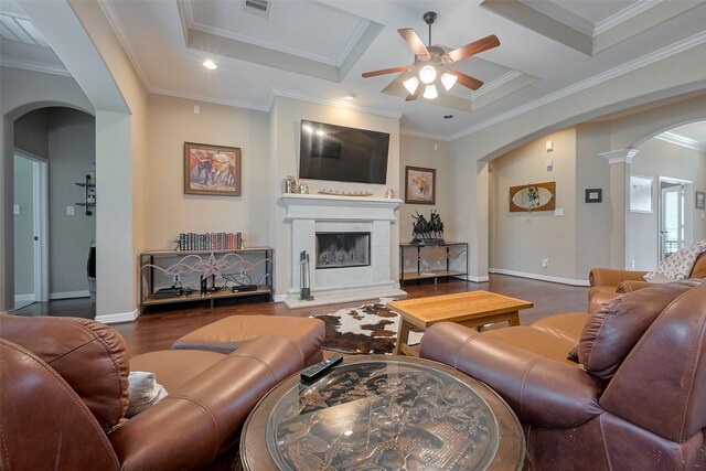 living room with a ceiling fan, crown molding, arched walkways, wood finished floors, and a fireplace with raised hearth