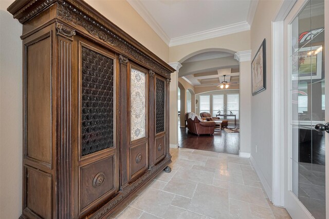 hall featuring crown molding, arched walkways, baseboards, and stone tile flooring