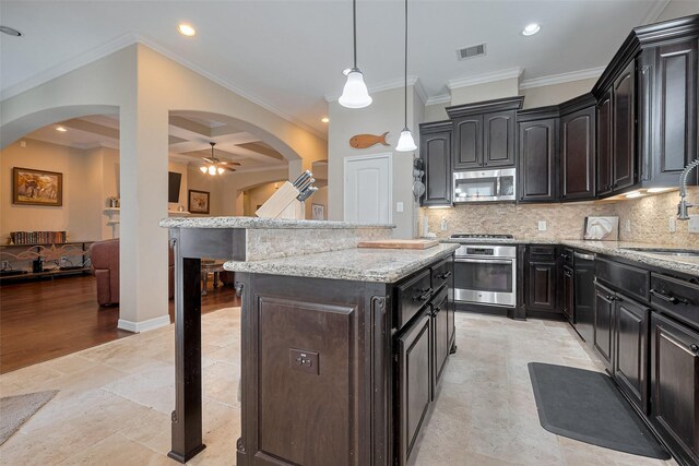 kitchen featuring visible vents, ornamental molding, a sink, stainless steel microwave, and arched walkways