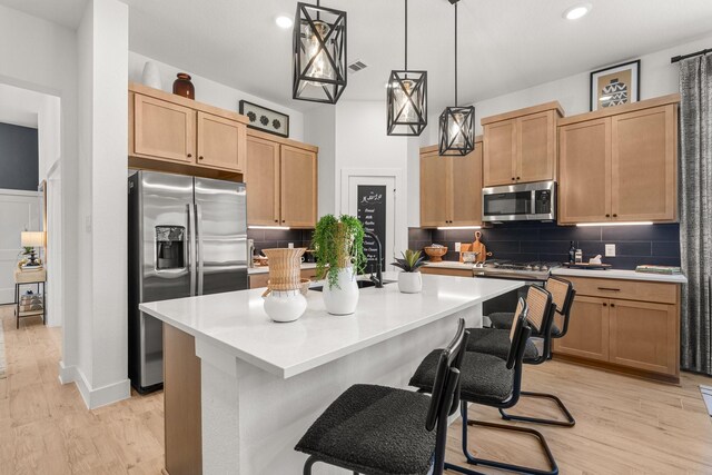 kitchen featuring light countertops, stainless steel appliances, an island with sink, and light wood-style flooring
