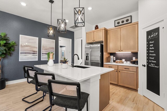 kitchen featuring a textured wall, stainless steel fridge, a sink, light wood finished floors, and light countertops