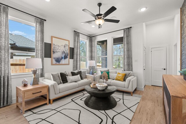 living area featuring ceiling fan, baseboards, and light wood finished floors