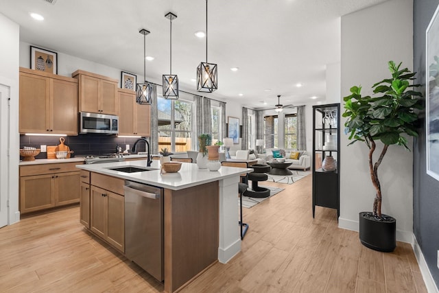 kitchen with appliances with stainless steel finishes, a sink, light countertops, light wood-style floors, and an island with sink
