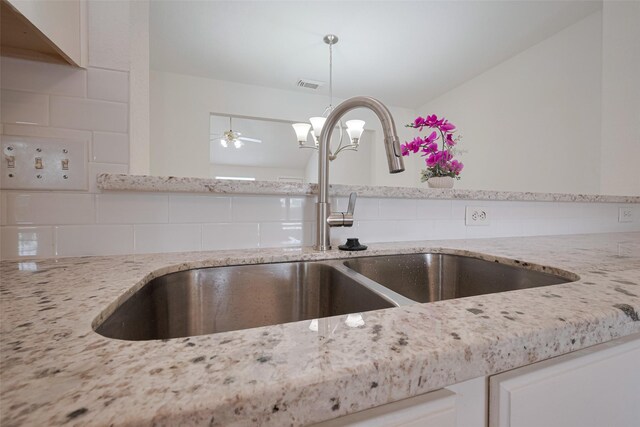 room details featuring visible vents, a sink, light stone counters, and tasteful backsplash