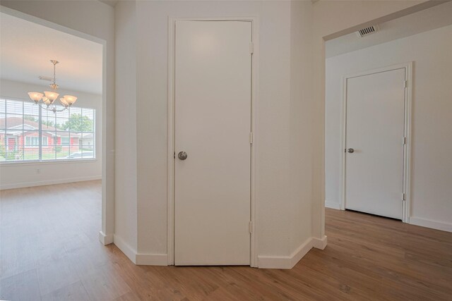 hallway with baseboards, wood finished floors, visible vents, and an inviting chandelier