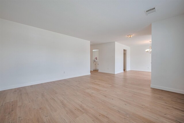 spare room featuring visible vents, light wood-style flooring, baseboards, and a notable chandelier
