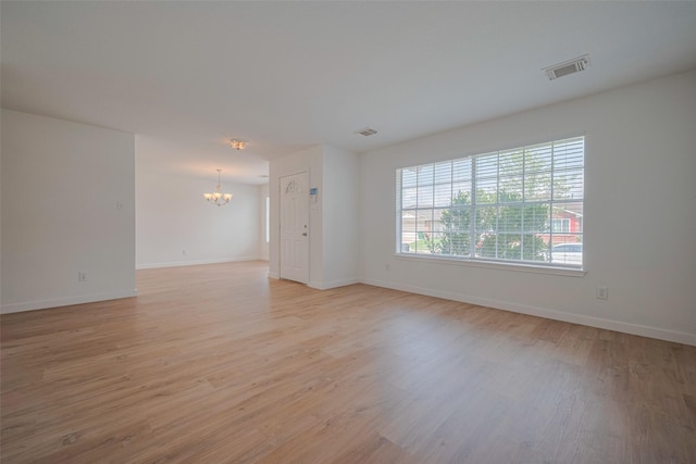 spare room featuring light wood-type flooring, baseboards, a notable chandelier, and visible vents