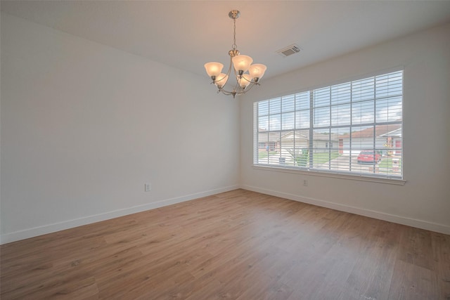 unfurnished room with visible vents, baseboards, wood finished floors, and an inviting chandelier