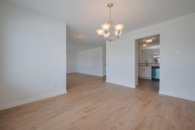 empty room featuring a sink, baseboards, light wood finished floors, and a chandelier