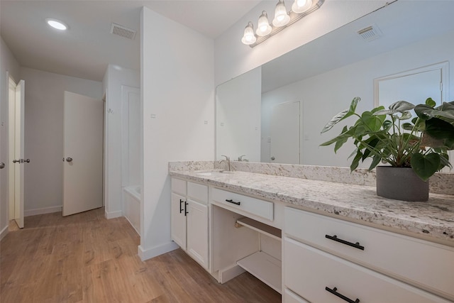 full bathroom featuring visible vents, wood finished floors, a tub to relax in, and vanity