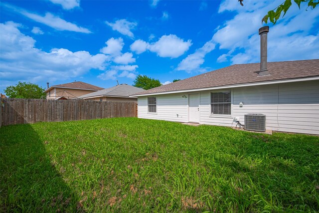 rear view of house featuring a yard, fence, central AC unit, and roof with shingles