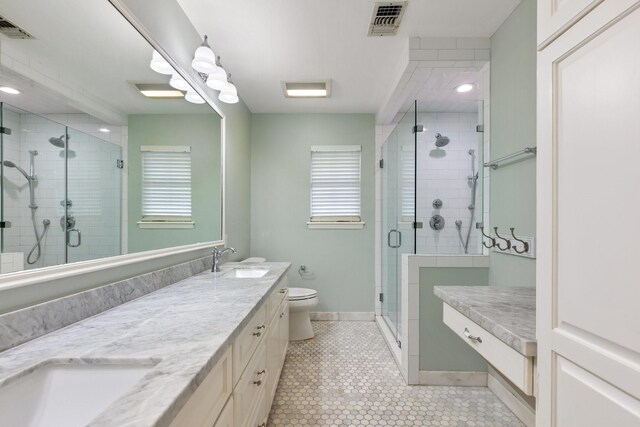 full bathroom with a sink, double vanity, toilet, a shower stall, and visible vents