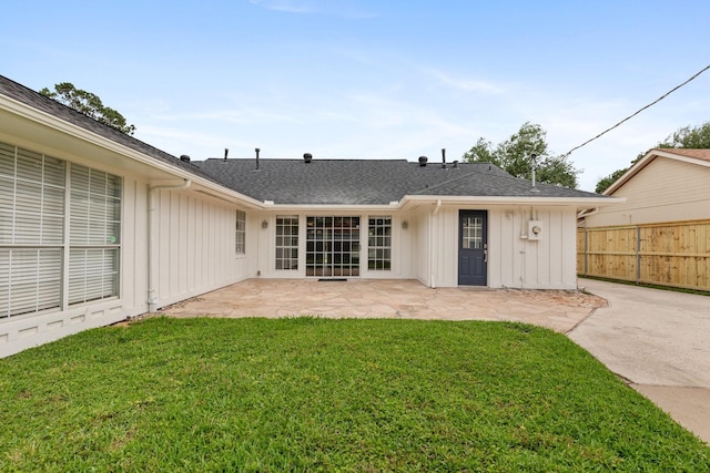 rear view of property featuring board and batten siding, roof with shingles, fence, a yard, and a patio