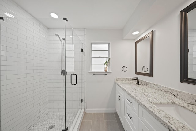 bathroom with double vanity, a sink, baseboards, and a stall shower