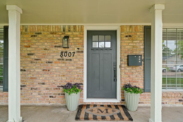 entrance to property featuring a porch and brick siding