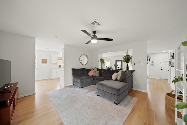 living area with visible vents, a ceiling fan, light wood finished floors, and baseboards