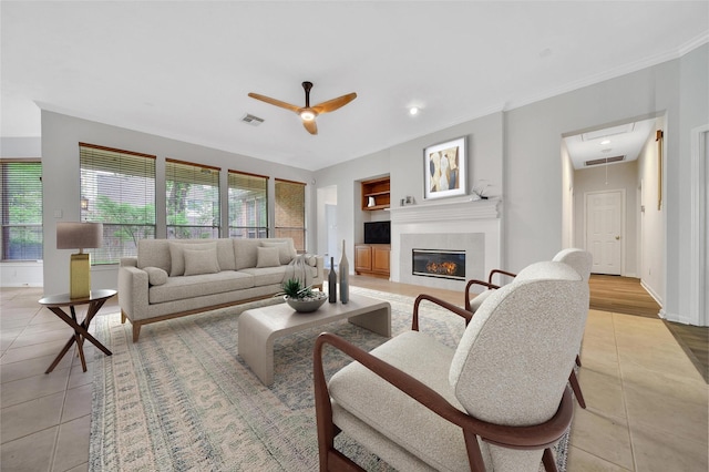living room with a ceiling fan, visible vents, a tiled fireplace, and light tile patterned floors