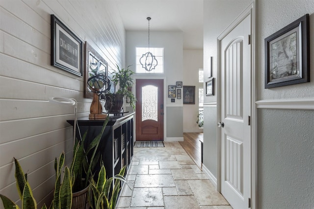 foyer entrance featuring baseboards, a chandelier, and stone tile floors