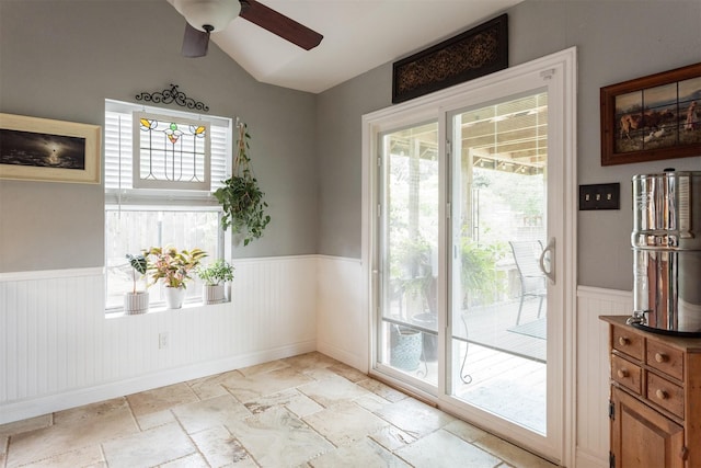 interior space featuring stone tile floors, ceiling fan, lofted ceiling, and a wainscoted wall
