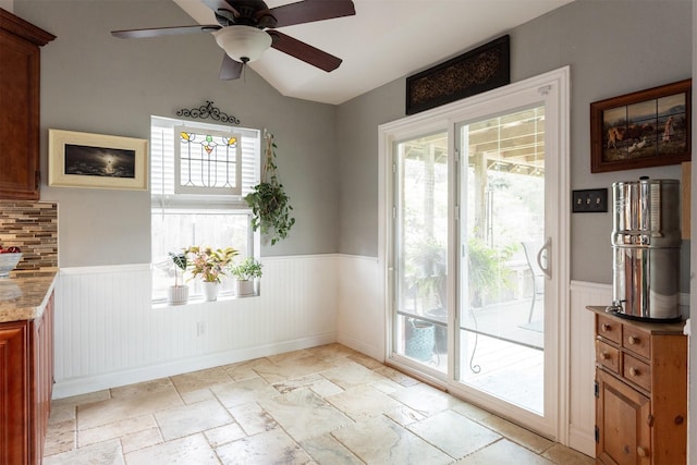 unfurnished dining area featuring stone tile floors, wainscoting, and ceiling fan