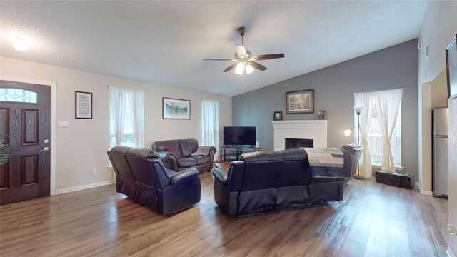 living area featuring a ceiling fan, light wood-style flooring, vaulted ceiling, and a fireplace