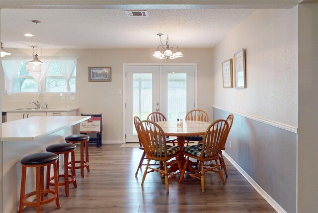 dining space with a textured ceiling, french doors, baseboards, light wood-type flooring, and visible vents