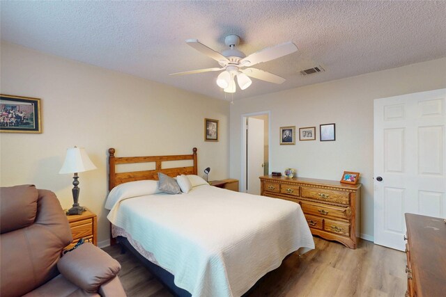 bedroom featuring ceiling fan, a textured ceiling, visible vents, baseboards, and light wood finished floors