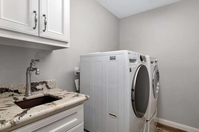 washroom with wood finished floors, cabinet space, a sink, baseboards, and washer and clothes dryer