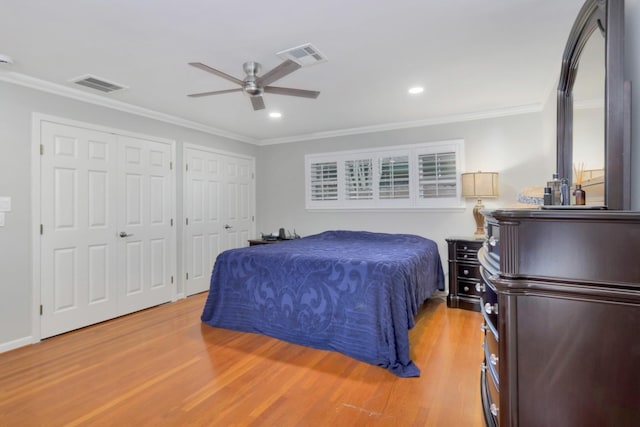 bedroom featuring visible vents, light wood finished floors, crown molding, and two closets