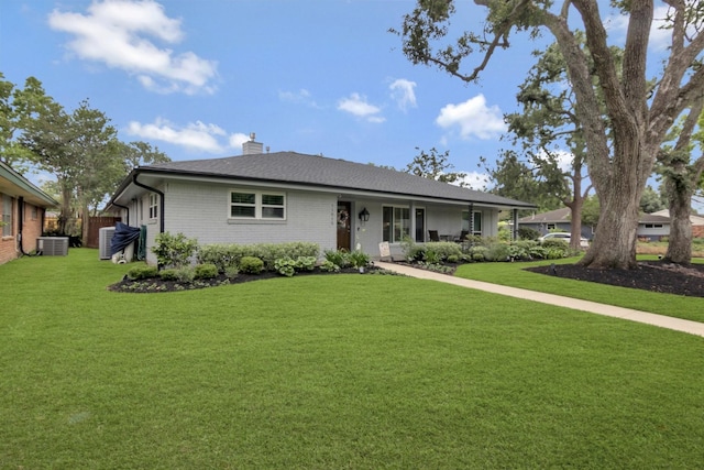 view of front of home with central air condition unit, a chimney, a front lawn, and brick siding