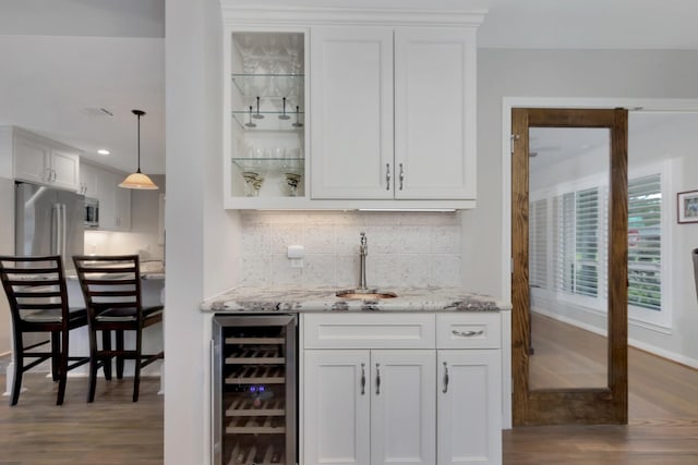 bar featuring dark wood-style flooring, beverage cooler, indoor wet bar, baseboards, and decorative backsplash