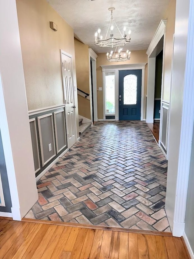 foyer with brick floor, a notable chandelier, and stairway