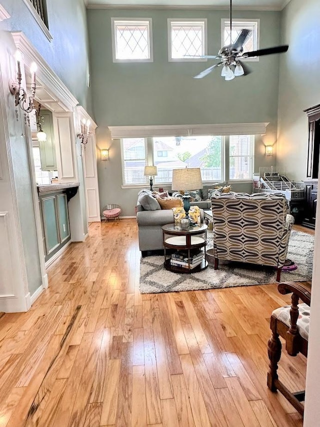 living area with a healthy amount of sunlight, a high ceiling, a ceiling fan, and light wood-type flooring