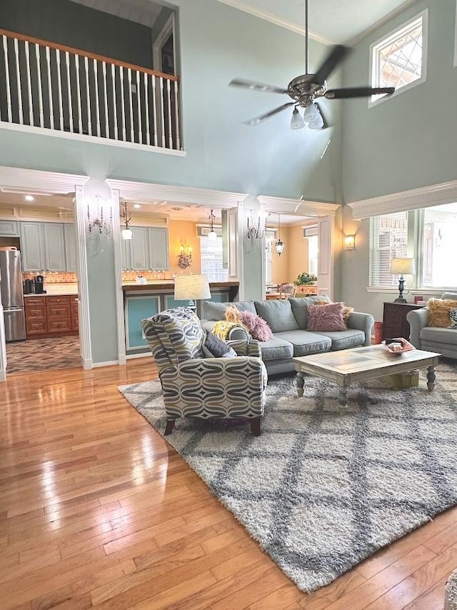 living area with ornamental molding, ceiling fan, a high ceiling, and hardwood / wood-style floors