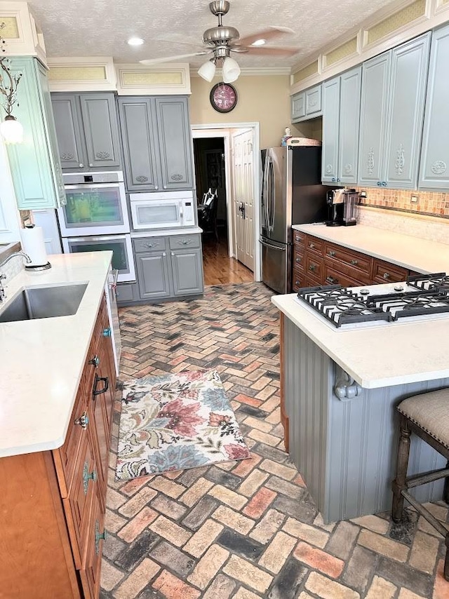 kitchen with a breakfast bar, brick floor, white appliances, light countertops, and a ceiling fan