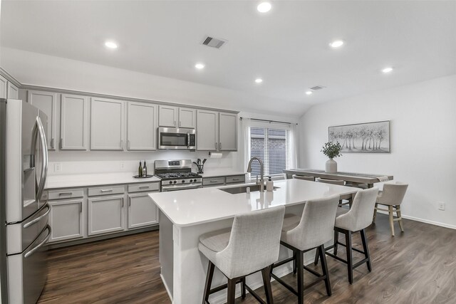 kitchen with a kitchen breakfast bar, visible vents, gray cabinetry, a sink, and stainless steel appliances