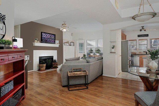 living room with baseboards, ceiling fan, a fireplace, and light wood-style flooring