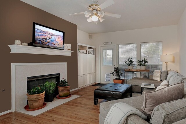 living room featuring baseboards, a ceiling fan, wood finished floors, and a tile fireplace