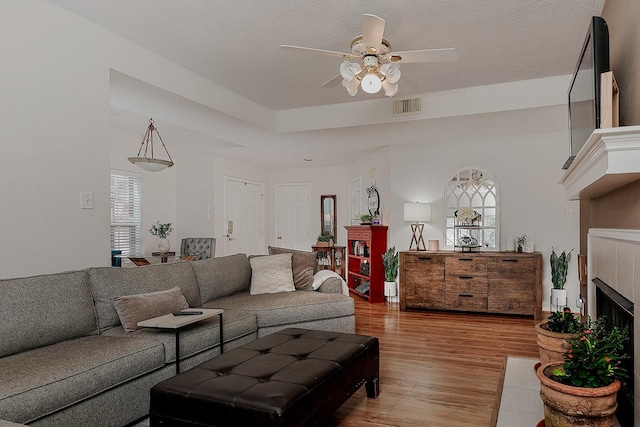 living area featuring ceiling fan, visible vents, light wood-style flooring, and a tile fireplace