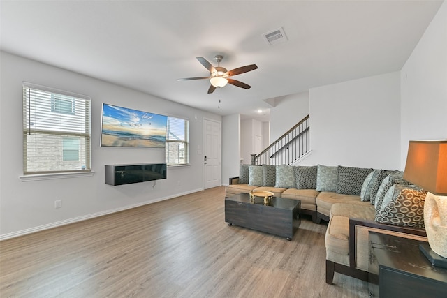 living room featuring ceiling fan, visible vents, wood finished floors, baseboards, and stairs
