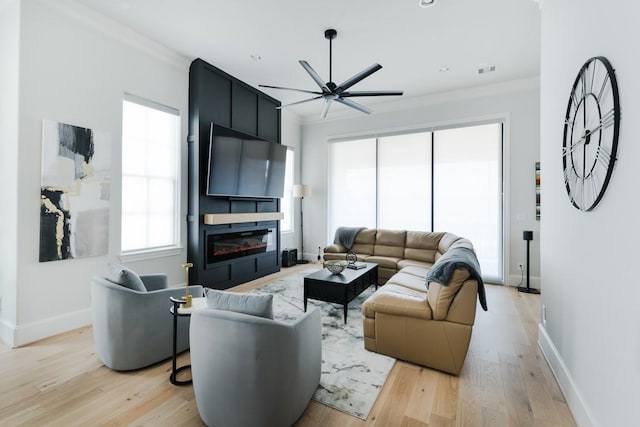 living area featuring baseboards, a ceiling fan, light wood finished floors, and a large fireplace