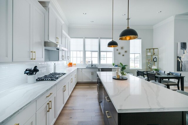 kitchen featuring a kitchen island, under cabinet range hood, a sink, a wealth of natural light, and stainless steel gas stovetop