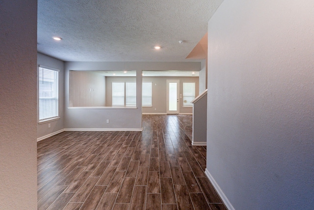 interior space featuring baseboards, a textured wall, a textured ceiling, and dark wood-type flooring