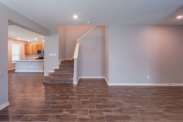 unfurnished living room featuring a textured ceiling, dark wood finished floors, stairs, baseboards, and recessed lighting
