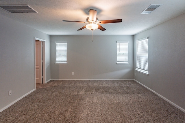 carpeted spare room with a ceiling fan, visible vents, and a healthy amount of sunlight
