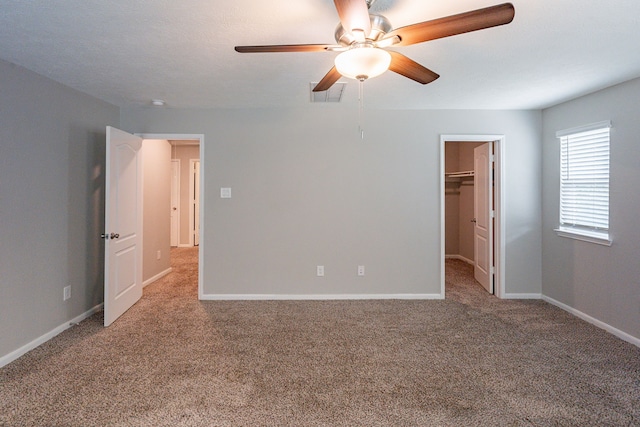 unfurnished bedroom featuring ceiling fan, a walk in closet, carpet, baseboards, and visible vents